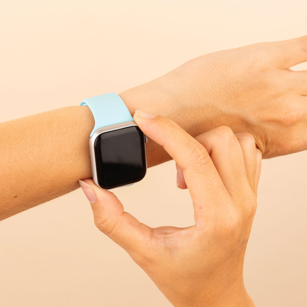 Hand with a light blue smartwatch. Hand touches the screen. Beige background.