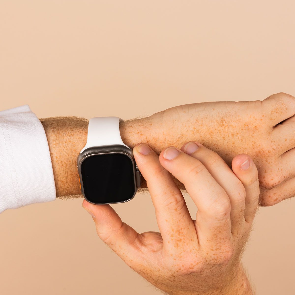 Person's arm with a white smartwatch. Hand touches the screen. Beige background.