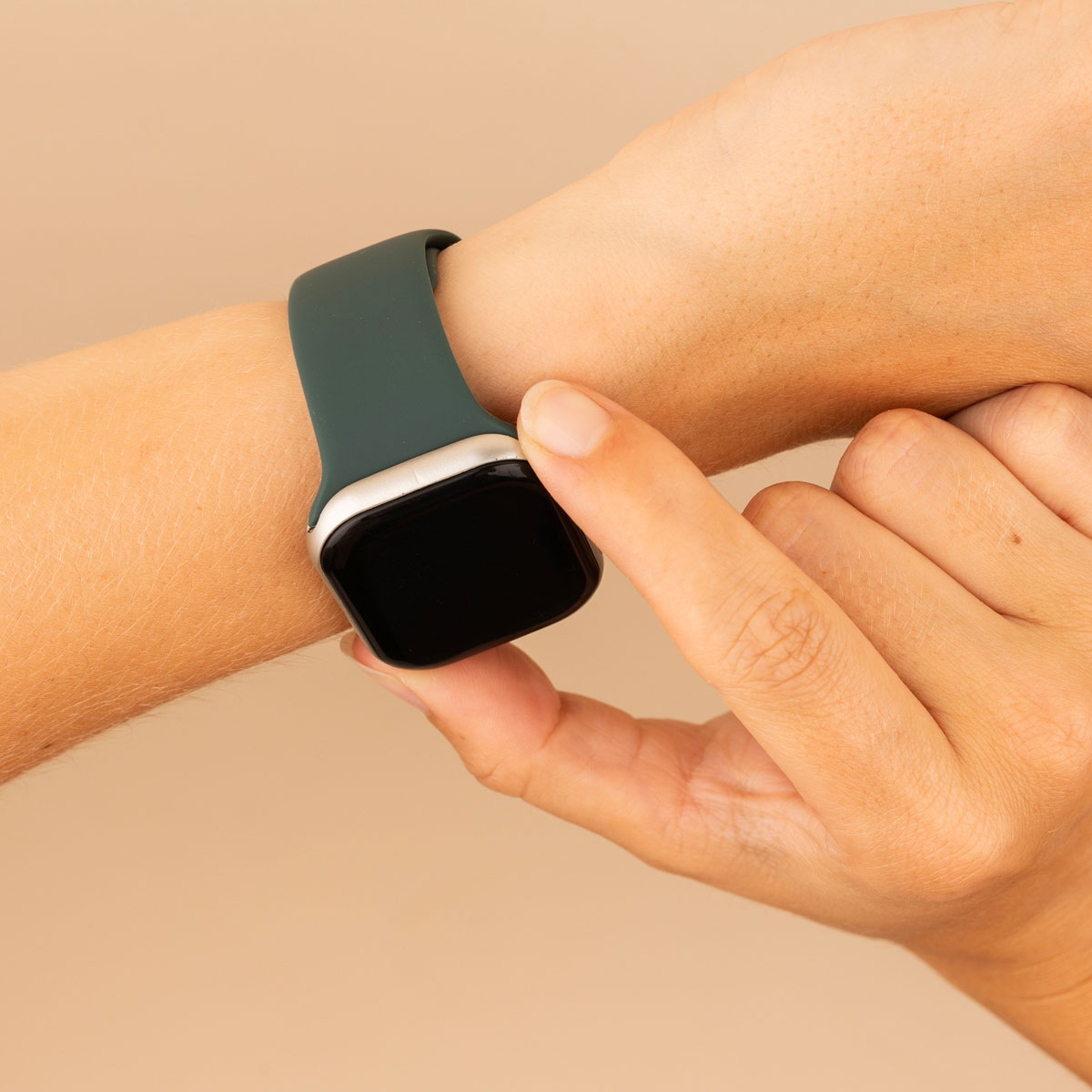 Hand with a dark green smartwatch. Hand touches the screen. Beige background.