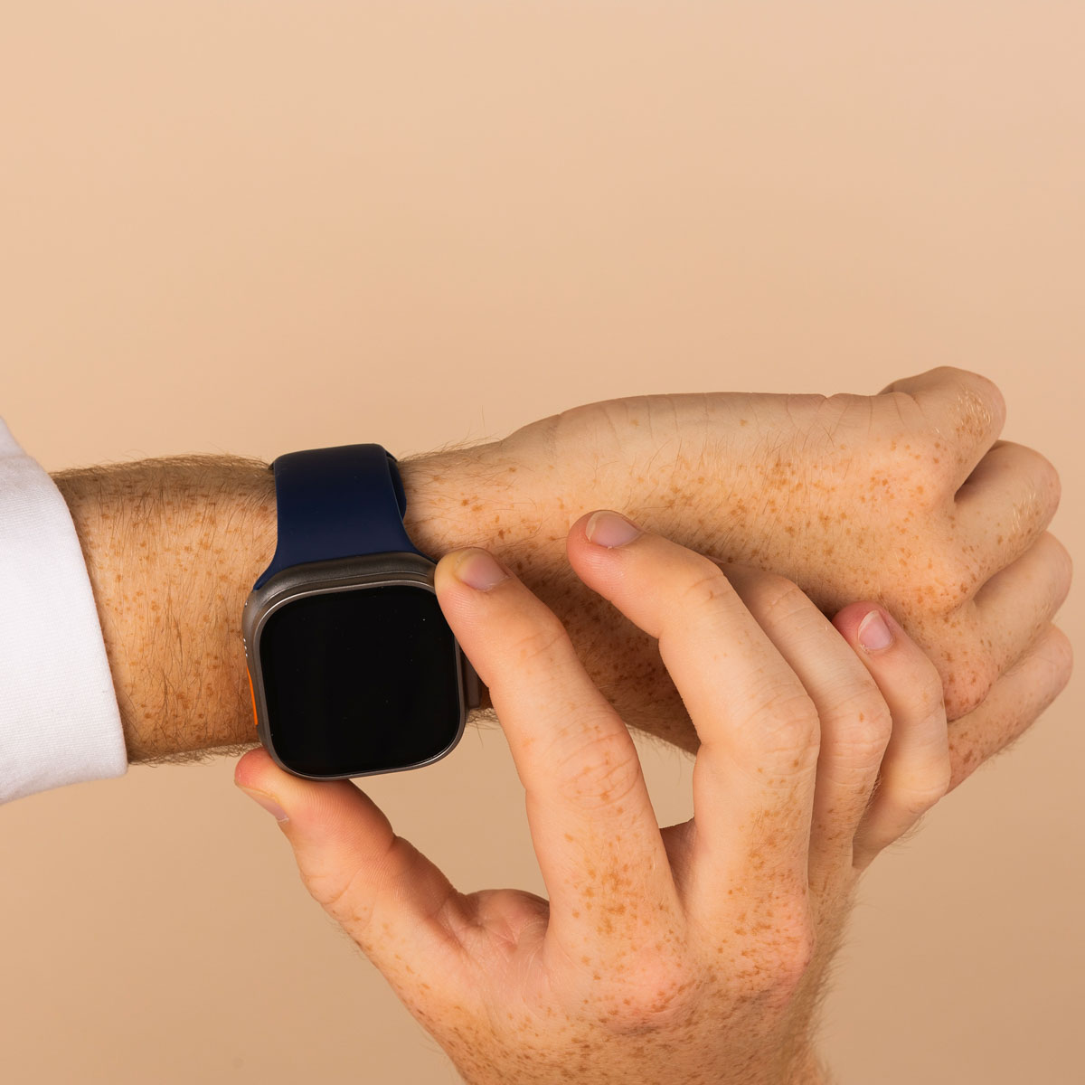 Person's arm with a blue smartwatch. Hand touches the screen. Beige background.