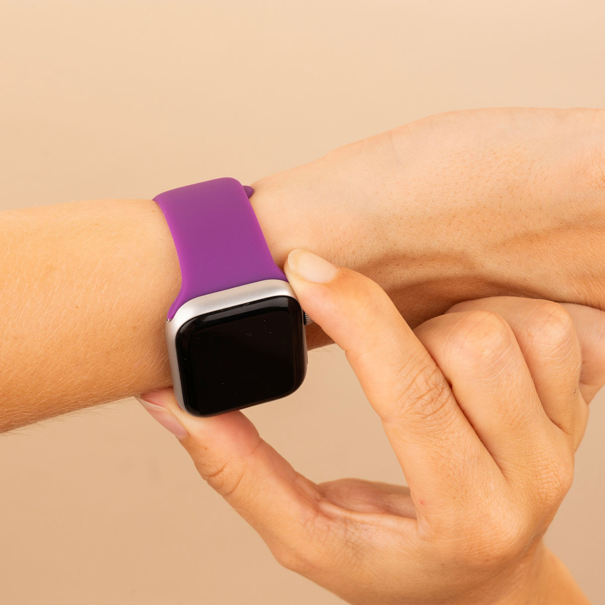 Hand with a purple smartwatch. Hand touches the screen. Beige background.