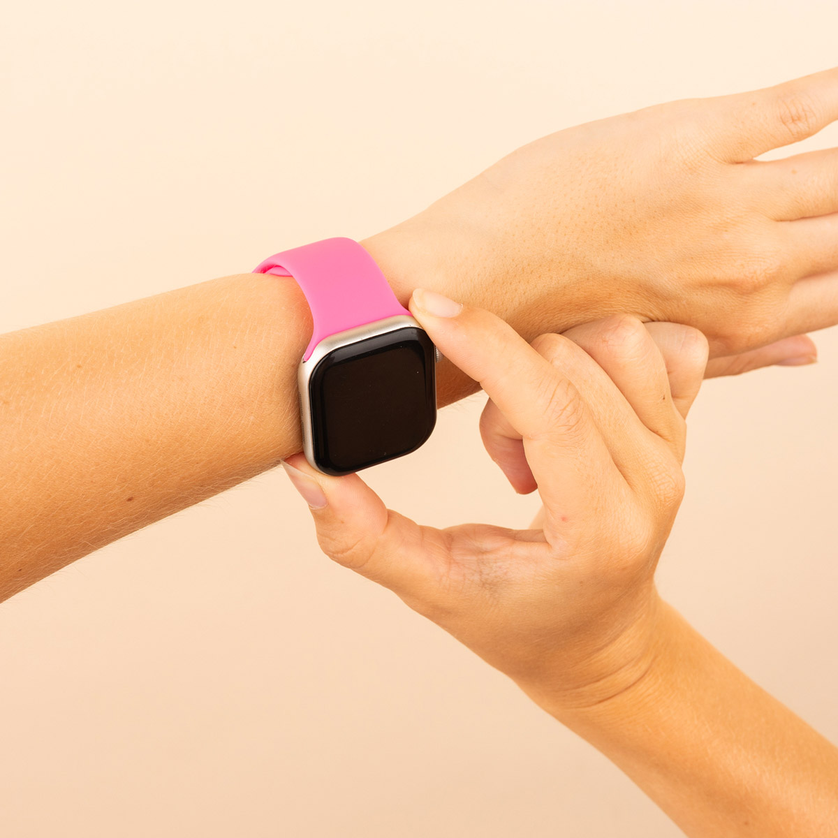Hand with a magenta smartwatch. Hand touches the screen. Beige background.
