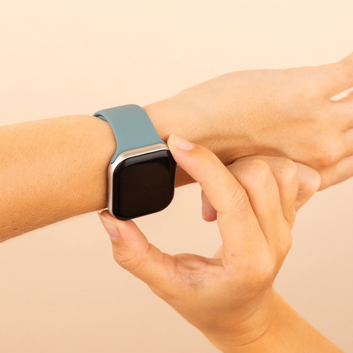 Hand with a teal smartwatch. Hand touches the screen. Beige background.