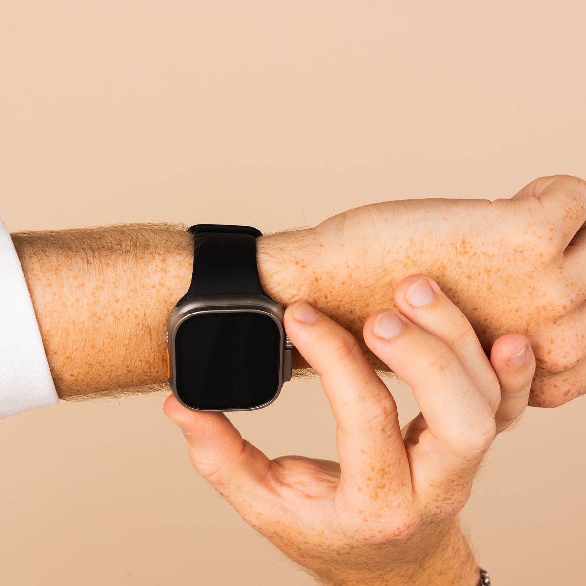 Person's arm with a black smartwatch. Hand touches the screen. Beige background.