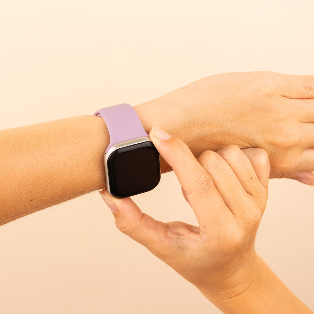 Hand with a lilac smartwatch. Hand touches the screen. Beige background.
