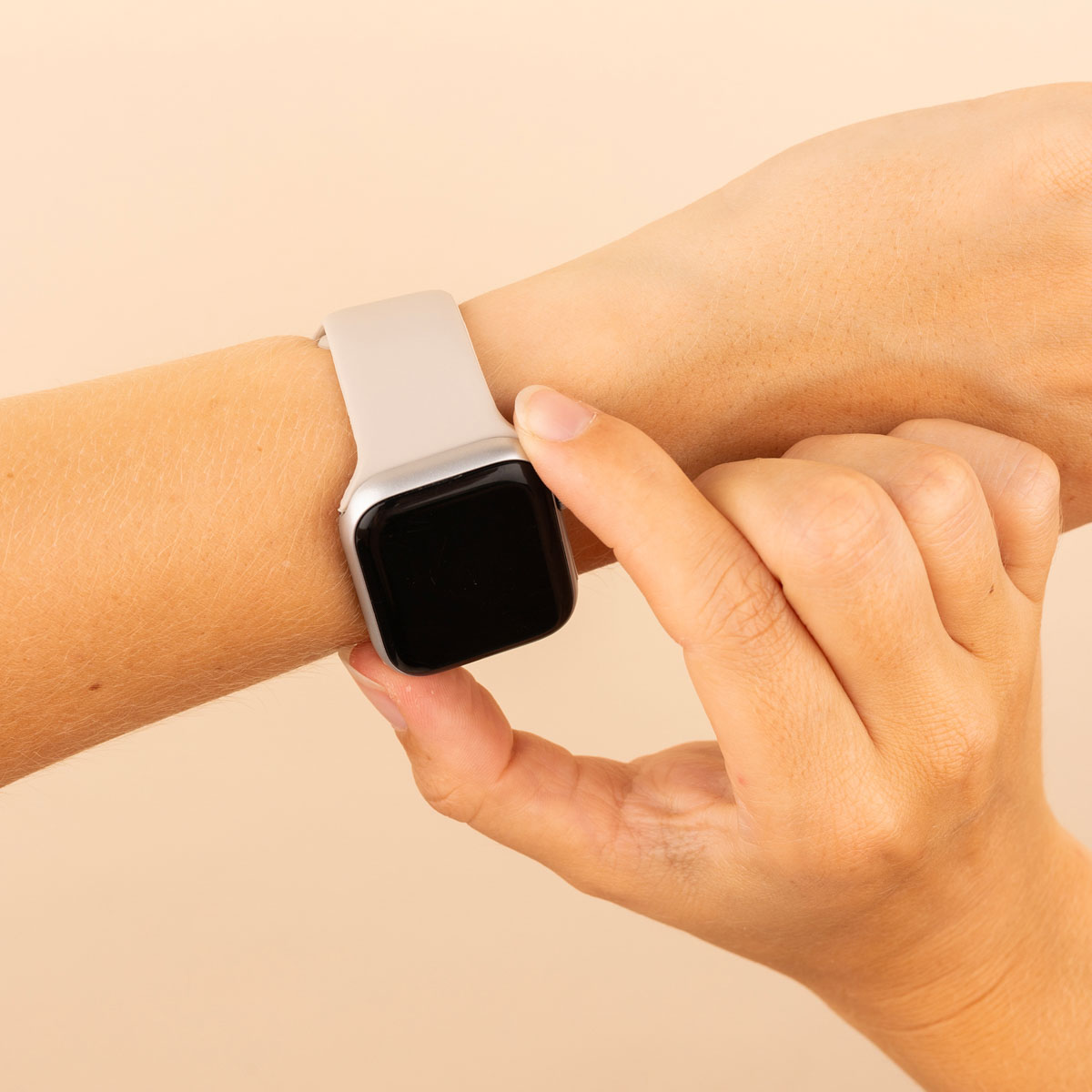 Hand with a light gray smartwatch. Hand touches the screen. Beige background.