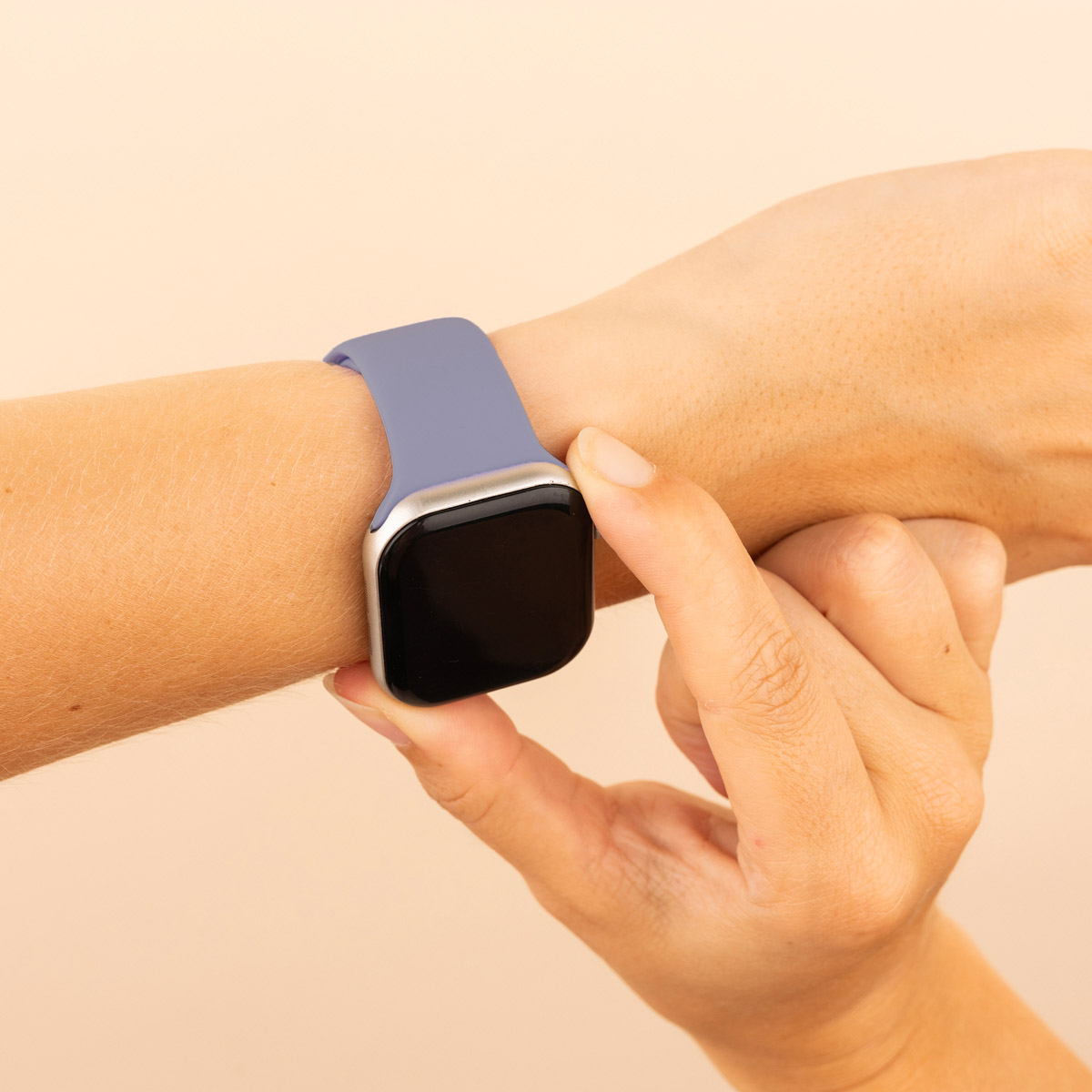 Hand with a periwinkle smartwatch. Hand touches the screen. Beige background.