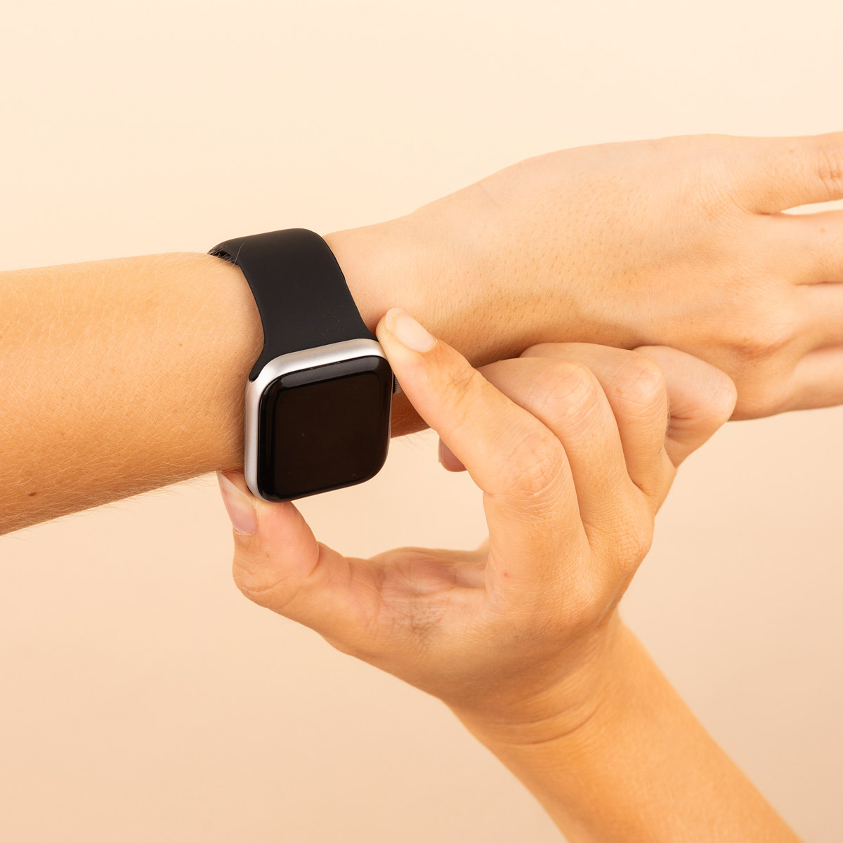Hand with a black smartwatch. Hand touches the screen. Beige background.