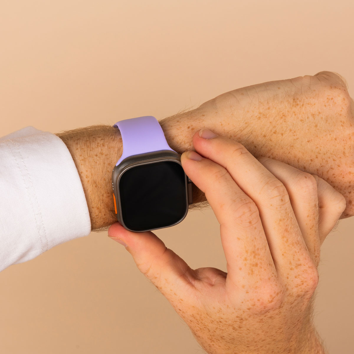 A hand with freckles wearing a smartwatch with a purple strap, on a beige background.