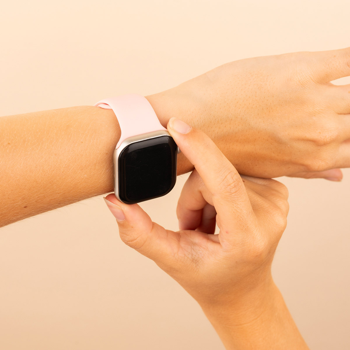 Hand with a pink smartwatch. Hand touches the screen. Beige background.