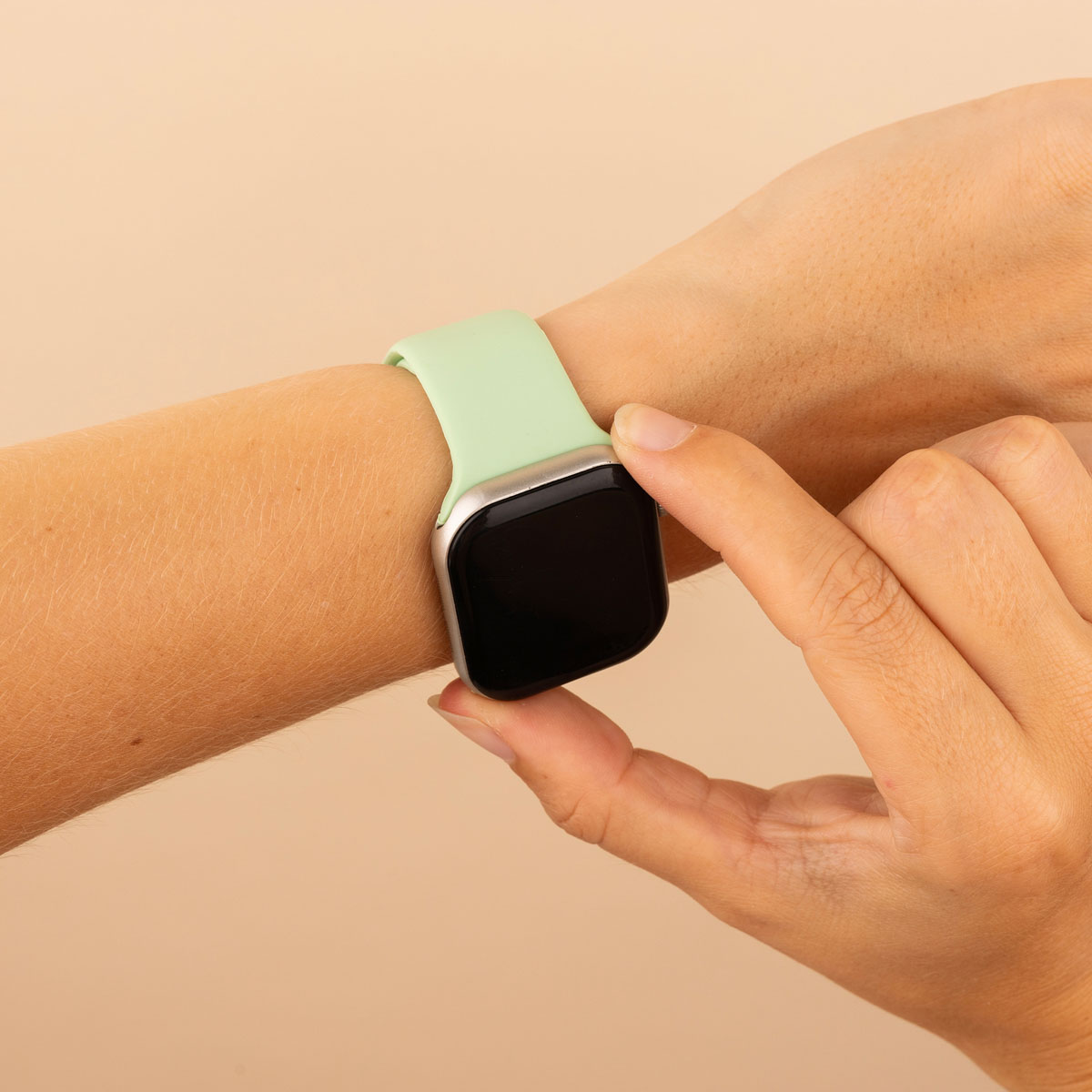 A wrist with a mint green smartwatch. A hand touches the watch face, the background is plain.