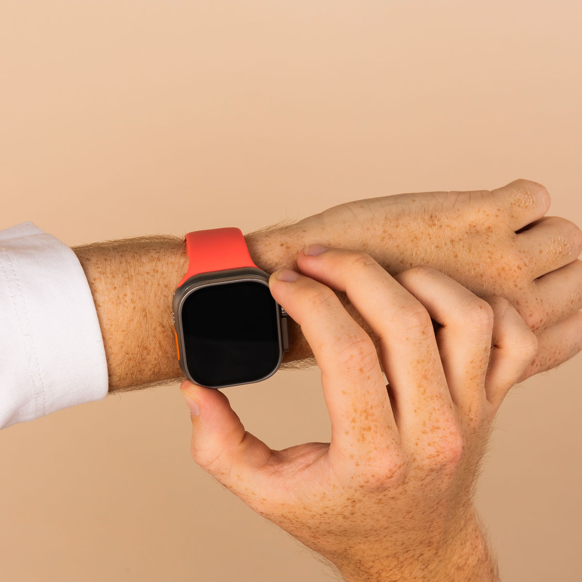 A person's wrist with a red smartwatch. A hand touches the watch face, background is plain.