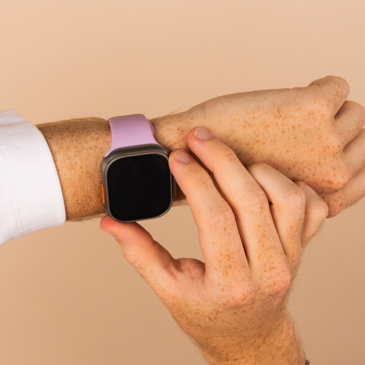 A person's wrist with a purple smartwatch. A hand touches the watch face, background is plain.