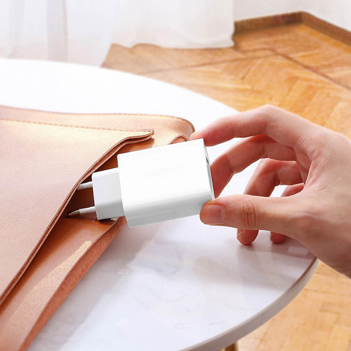 Ręka trzyma białą ładowarkę obok różowej torby na białym tle.