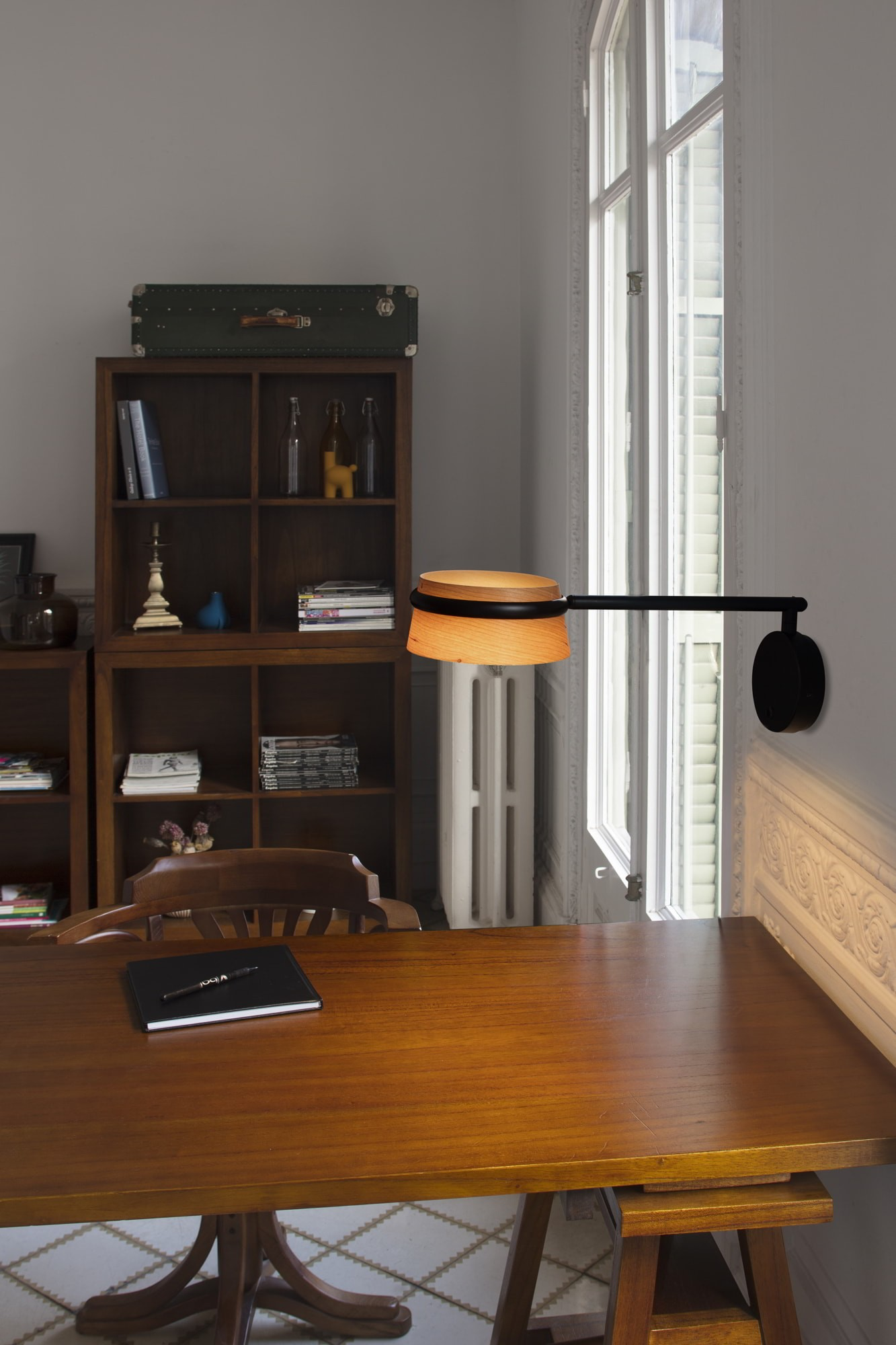 Una lampada da scrivania con paralume in legno è accesa. Una scrivania con taccuino e penna in primo piano.