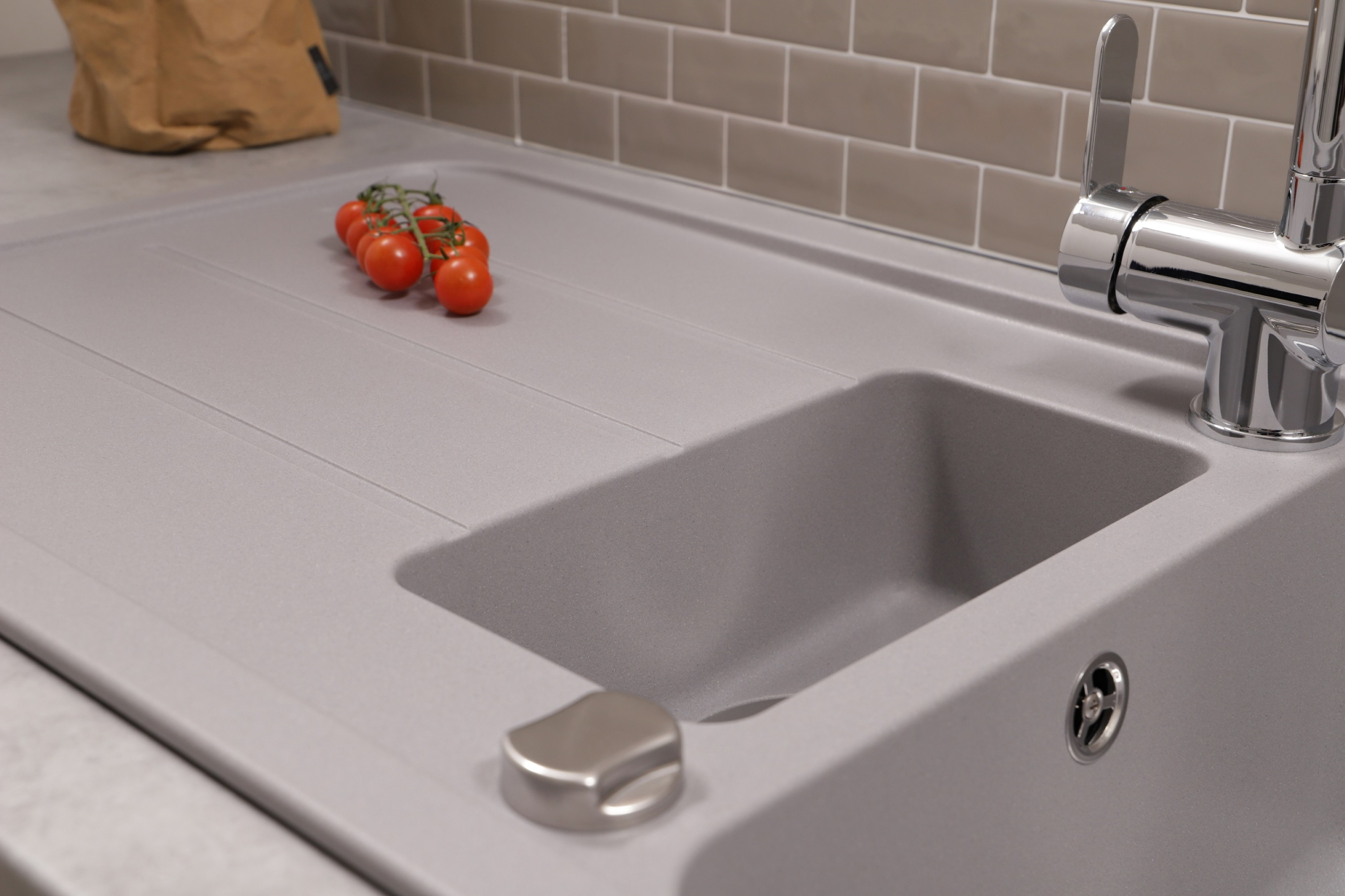 Ein graues Waschbecken mit Tomaten und einem Wasserhahn. Im Hintergrund eine Papiertüte.