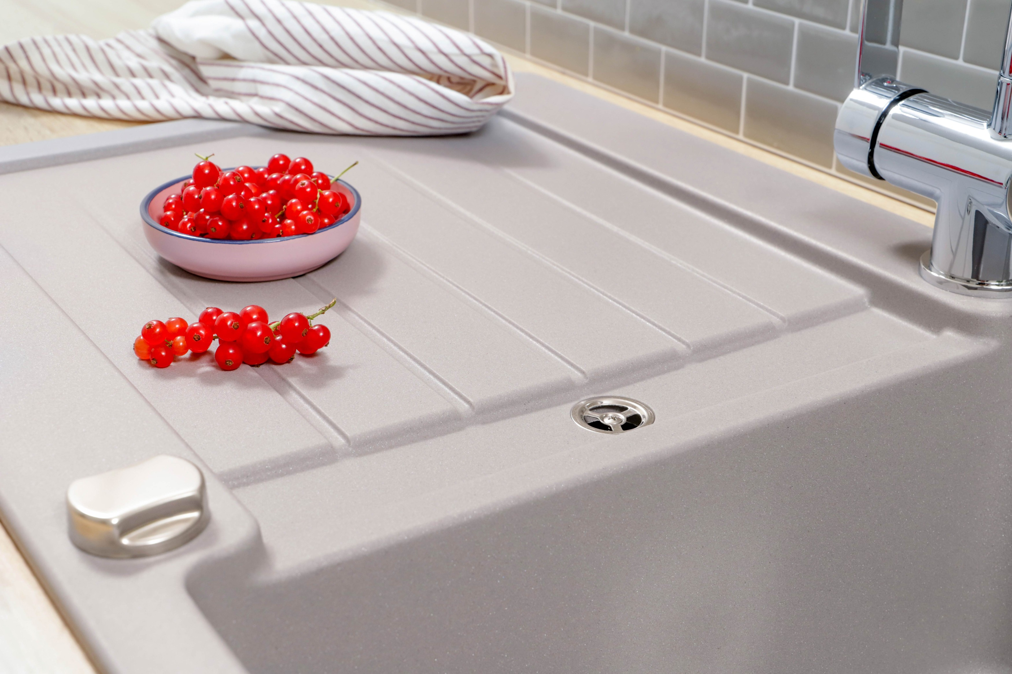 Graues Waschbecken mit roten Johannisbeeren in einer rosa Schüssel und einem gestreiften Handtuch im Hintergrund.