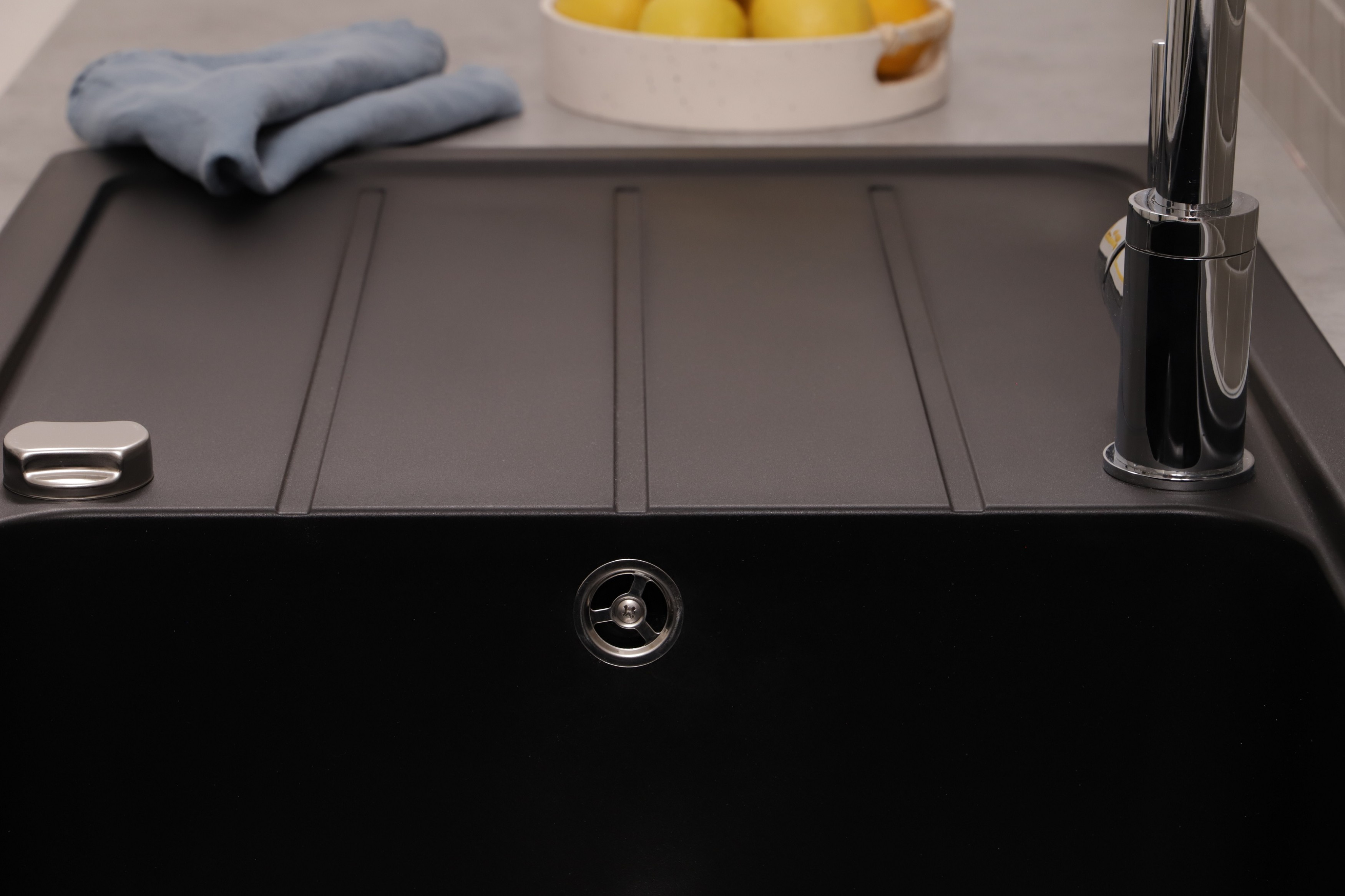 Lavello nero con rubinetto a destra e panno blu e limoni in una ciotola sullo sfondo.
