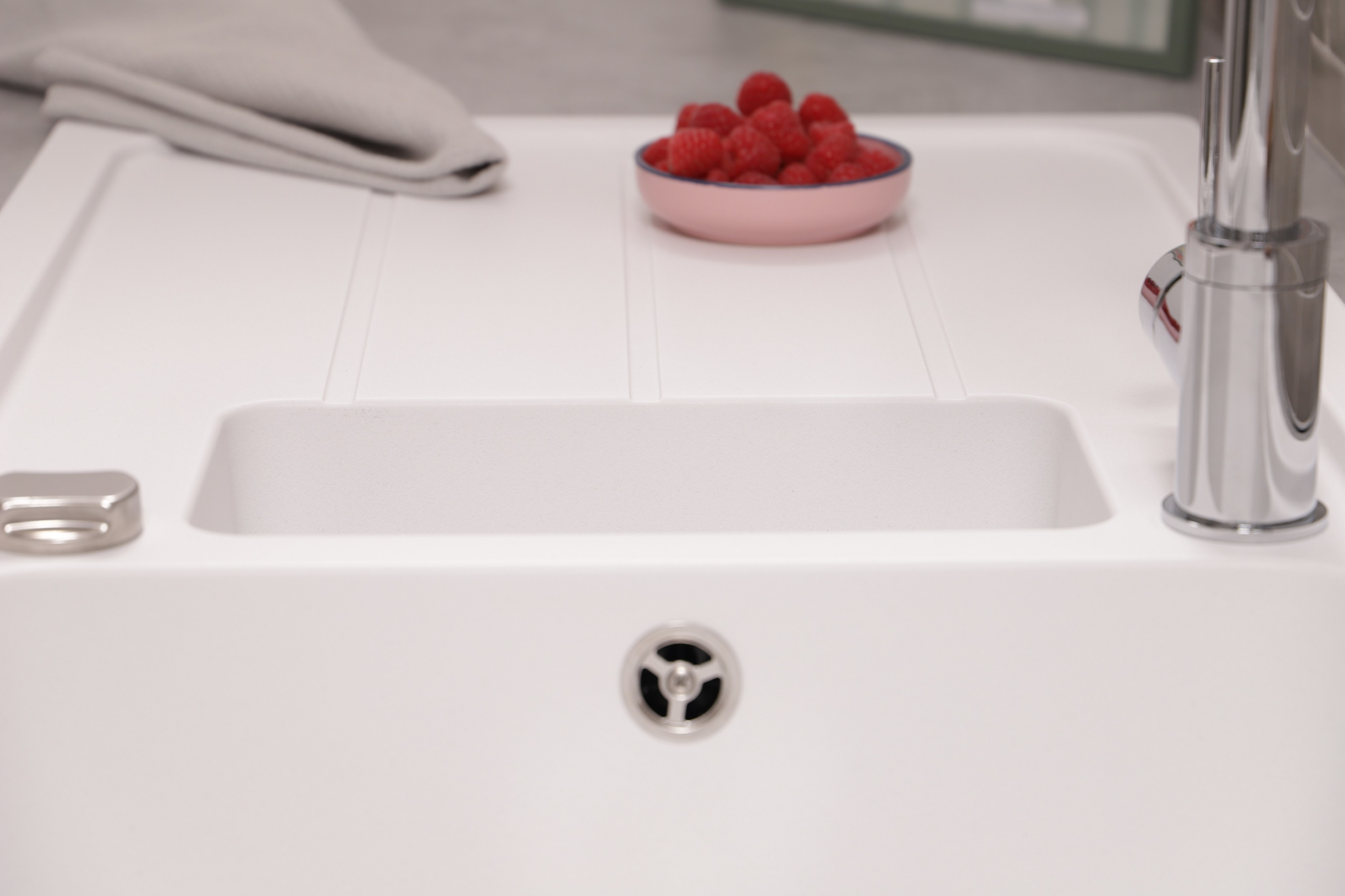 Ein weißes Waschbecken mit Abfluss, einer Chromarmatur und einer kleinen Schüssel mit Himbeeren.