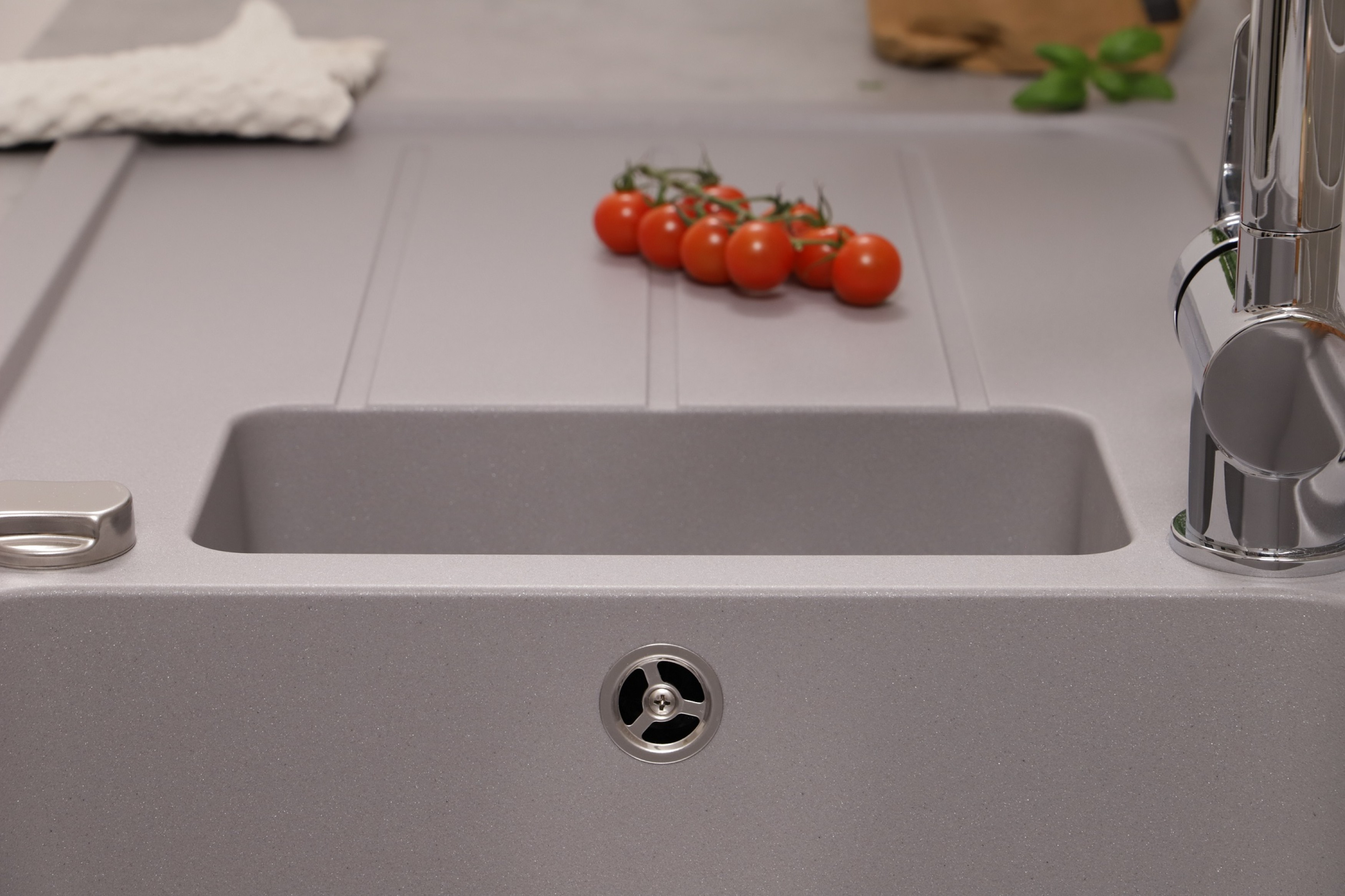 Graues Waschbecken mit Wasserhahn, einer Reihe von Tomaten und einem Abfluss. Der Hintergrund ist unscharf.