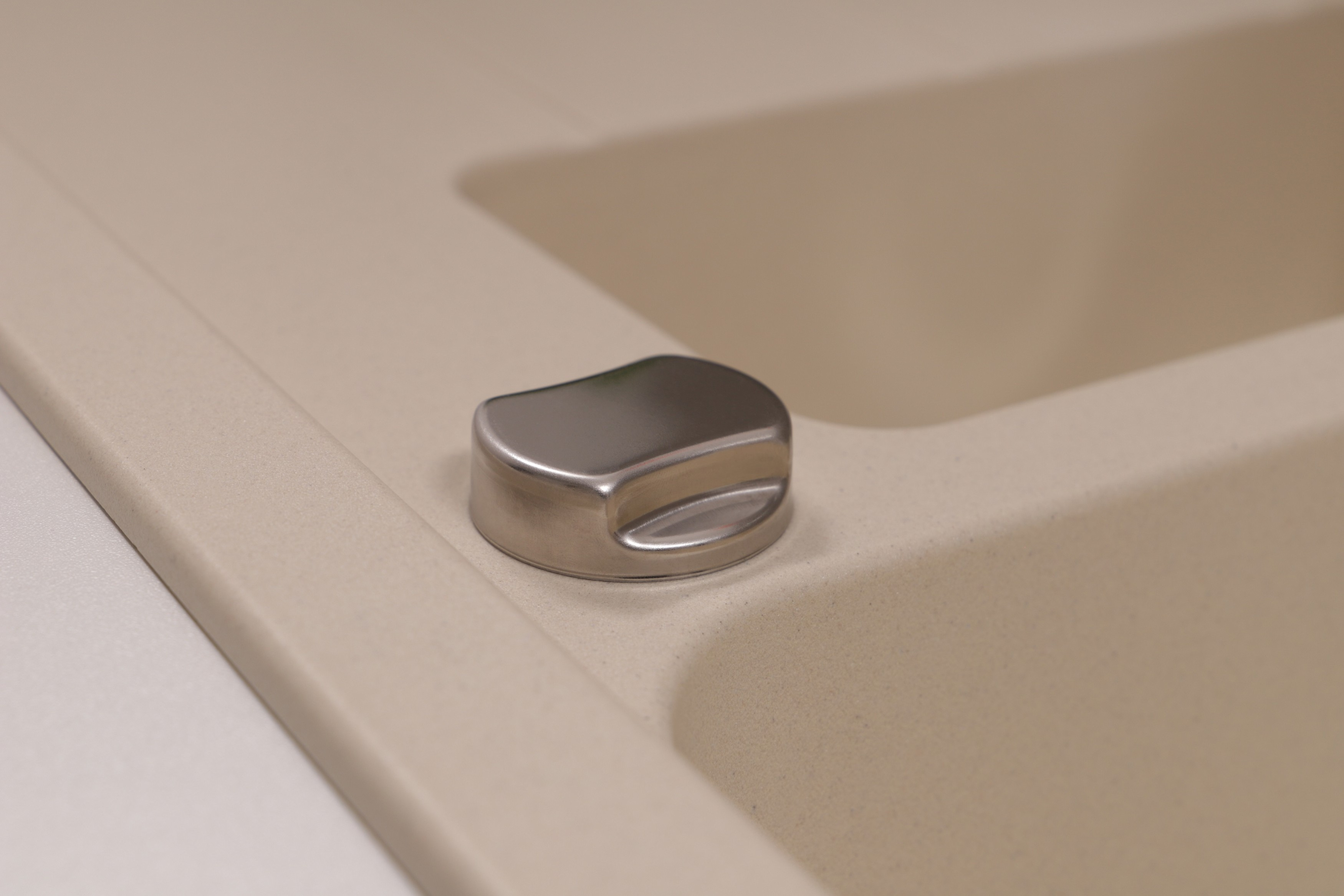 Nahaufnahme eines beigen Waschbeckens mit einem glänzenden Metallknopf. Das Waschbecken ist sauber und leer.