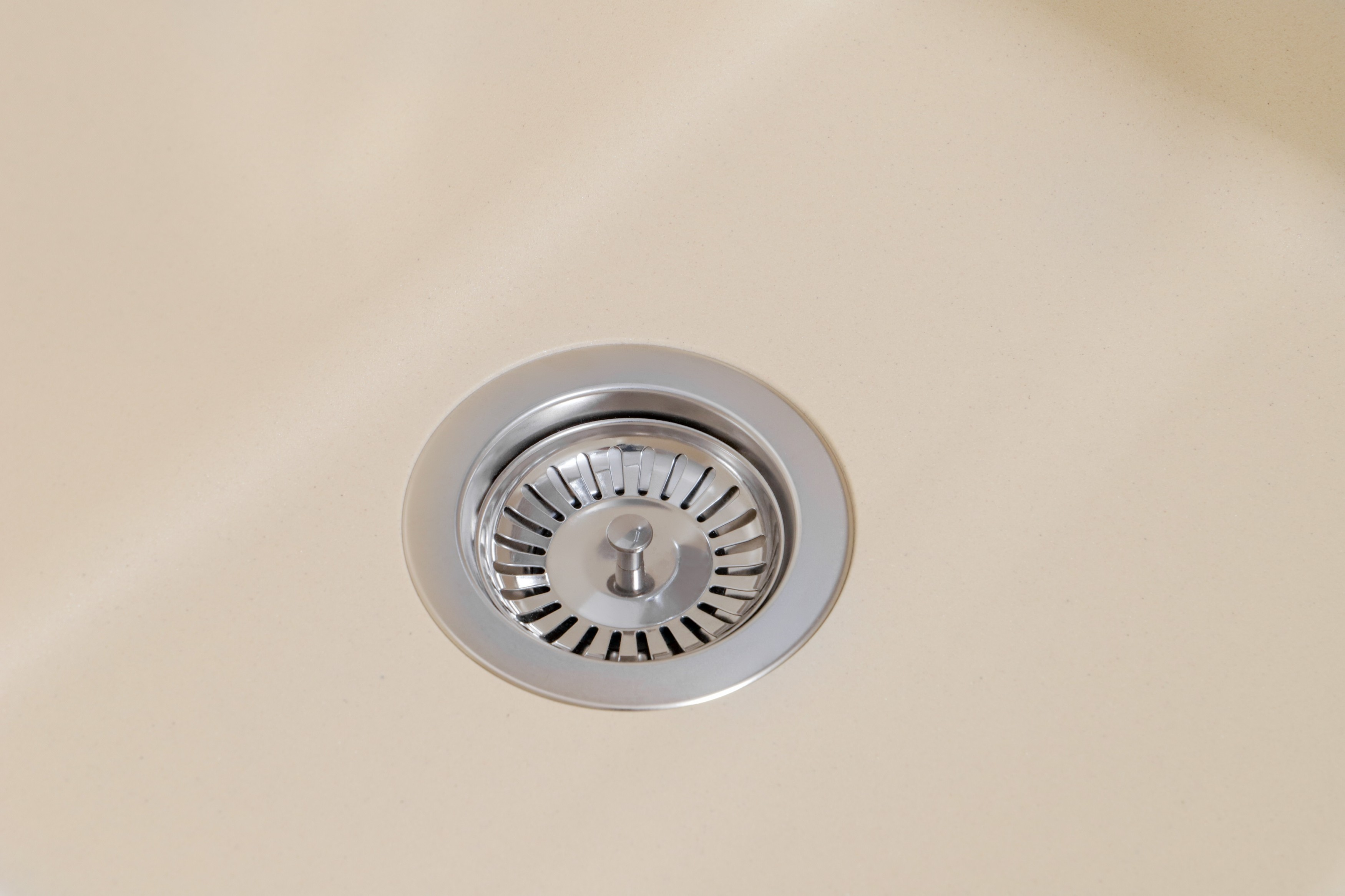 Nahaufnahme eines beigen Waschbeckenablaufs mit glänzender Metallabdeckung. Das Waschbecken ist sauber.