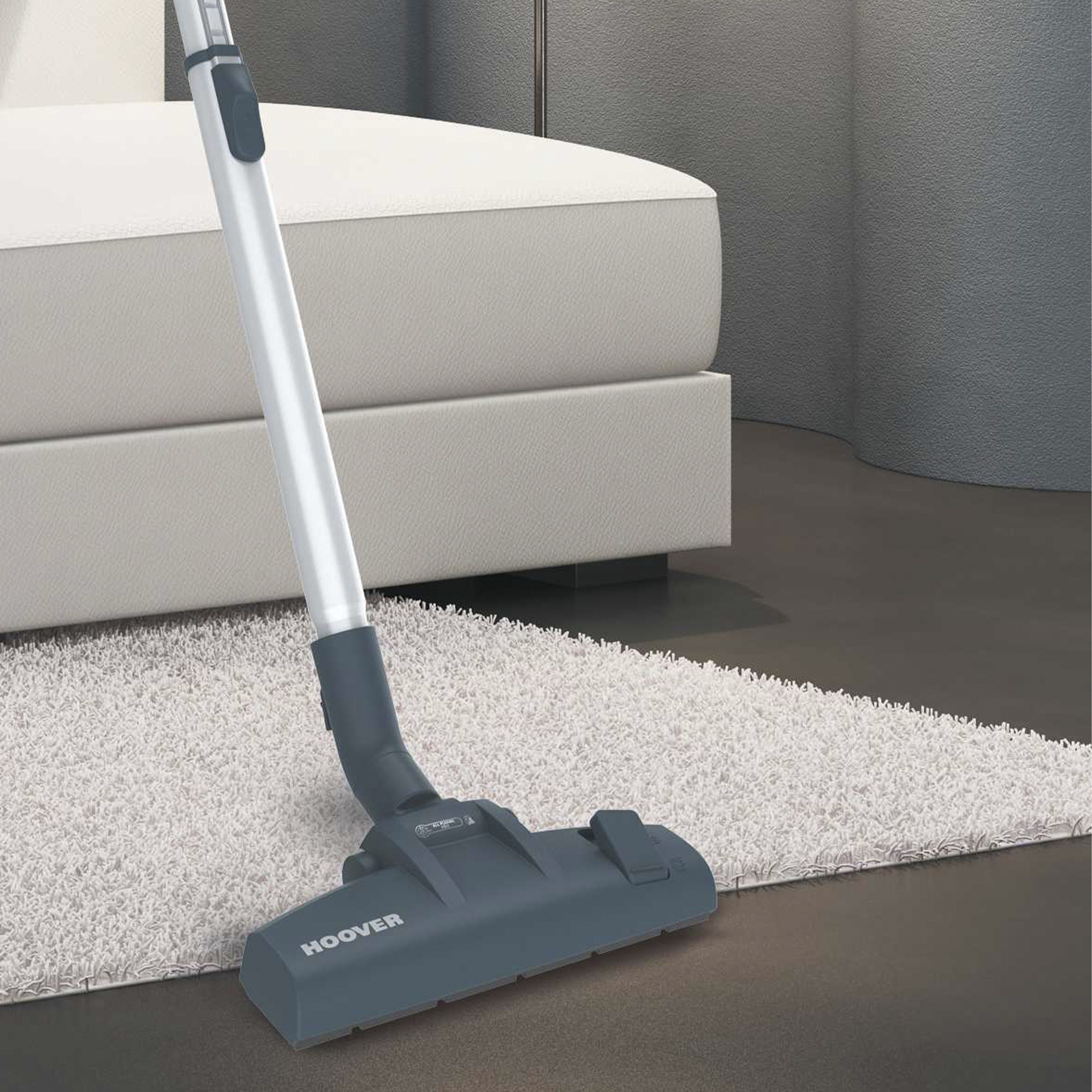 Głowica odkurzacza Hoover na jasnym dywanie. W tle łóżko. Widoczne jest logo Hoover.