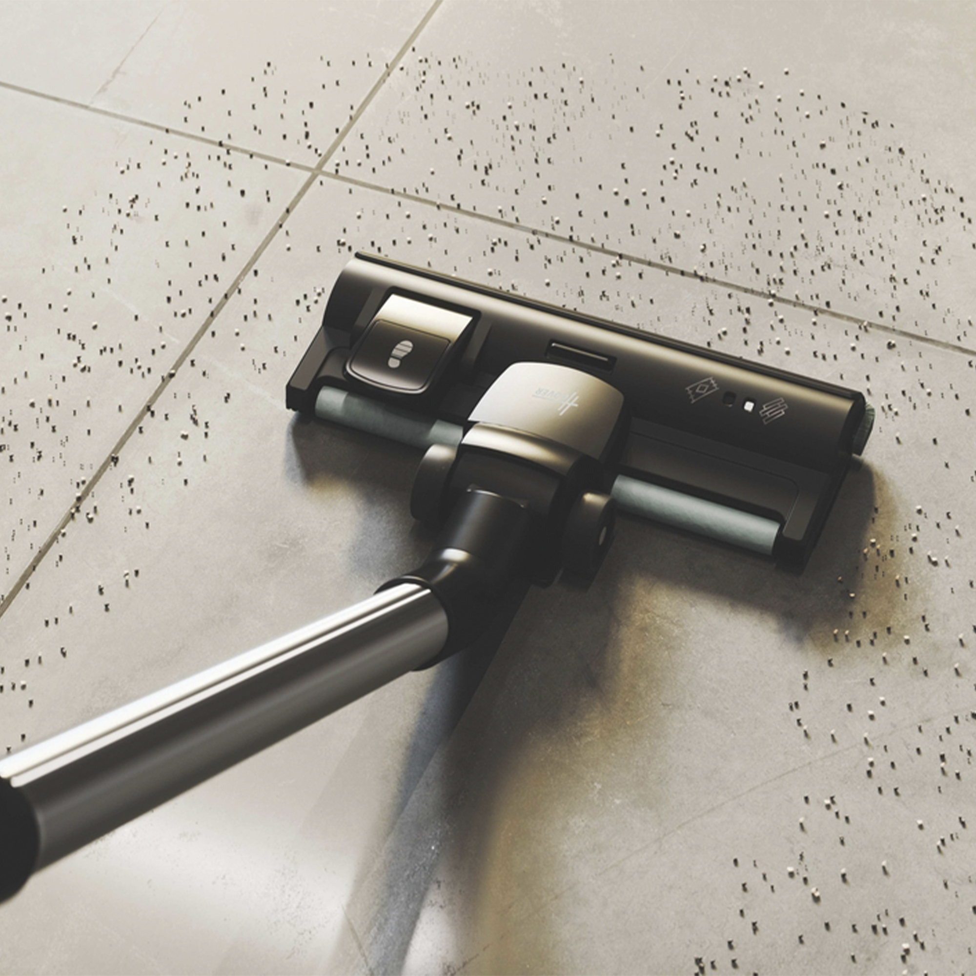 Głowica odkurzacza znajduje się na podłodze wyłożonej kafelkami, czyszcząc. Podłoga jest szara i pokryta brudem.