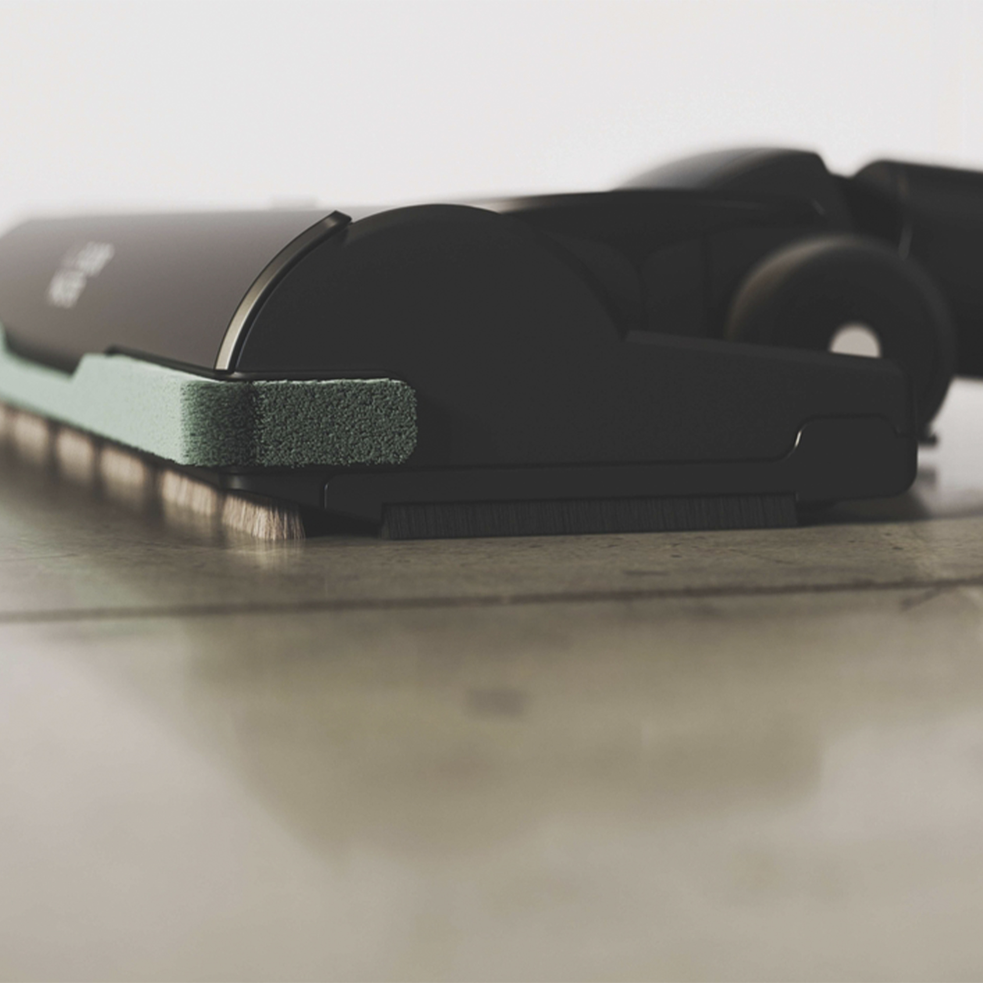 Zbliżenie czarnej głowicy odkurzacza z zieloną szczotką na kafelkach.