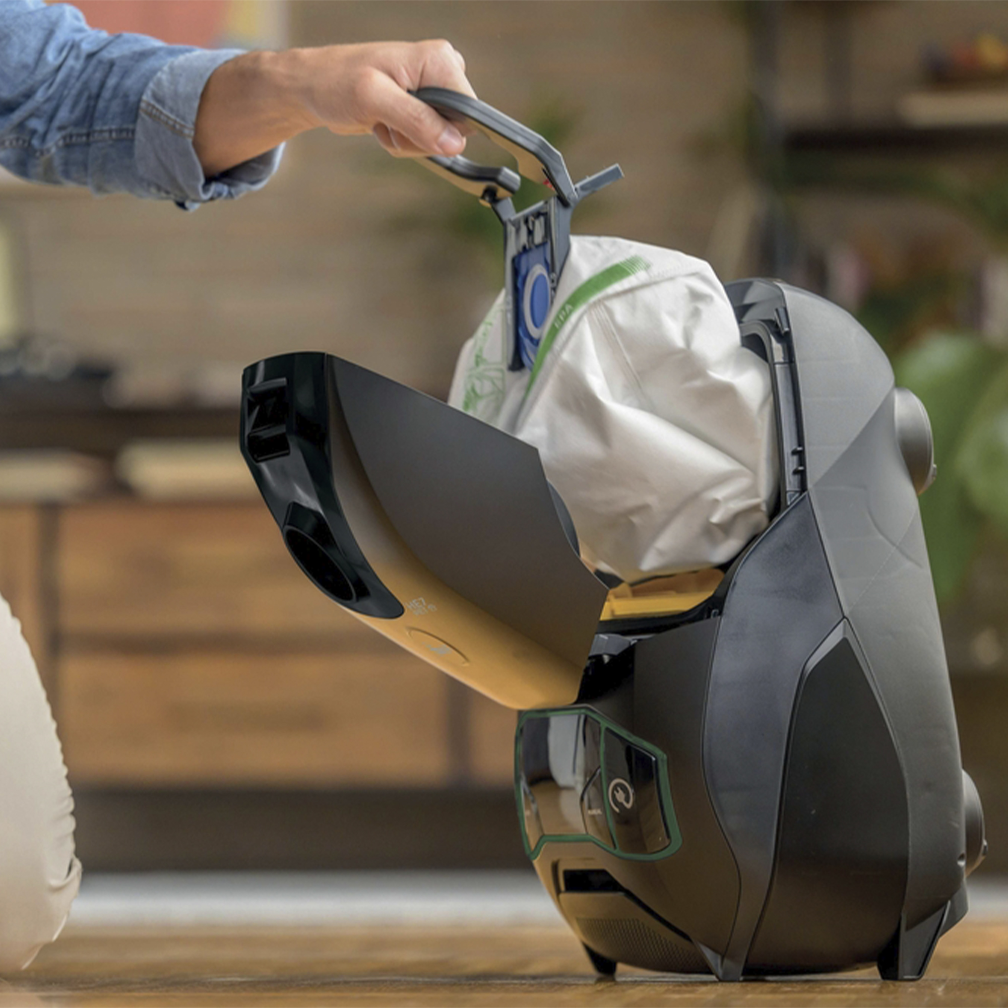 Osoba wyjmuje worek do odkurzacza z czarnego odkurzacza. Worek jest biały.