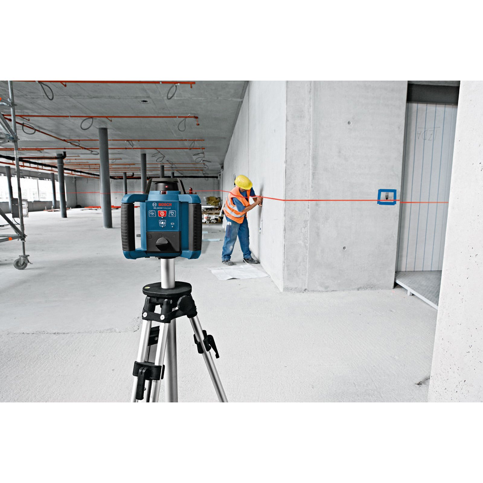 Eine Baustelle mit einem Laser-Nivelliergerät auf einem Stativ. Ein Arbeiter in einer Weste richtet eine rote Laserlinie aus.