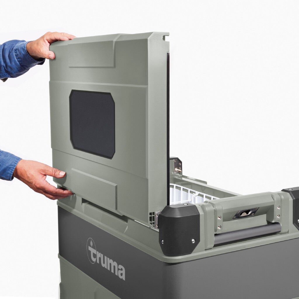 A person's hands opening the top of a cooler. The cooler is gray with a Truma logo.