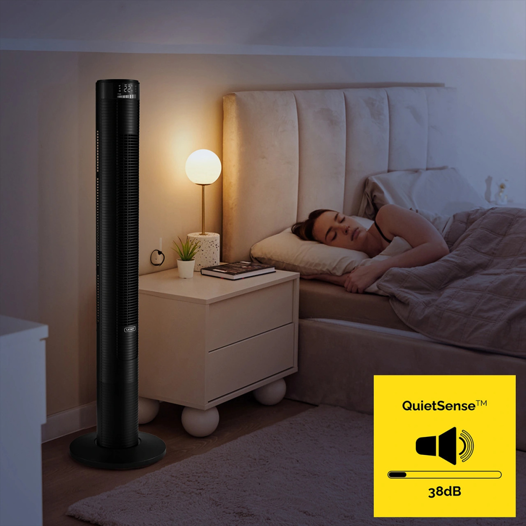 Czarny wentylator wieżowy z cyfrowym wyświetlaczem obok łóżka. Kobieta śpi w łóżku. Widoczne logo QuietSense.