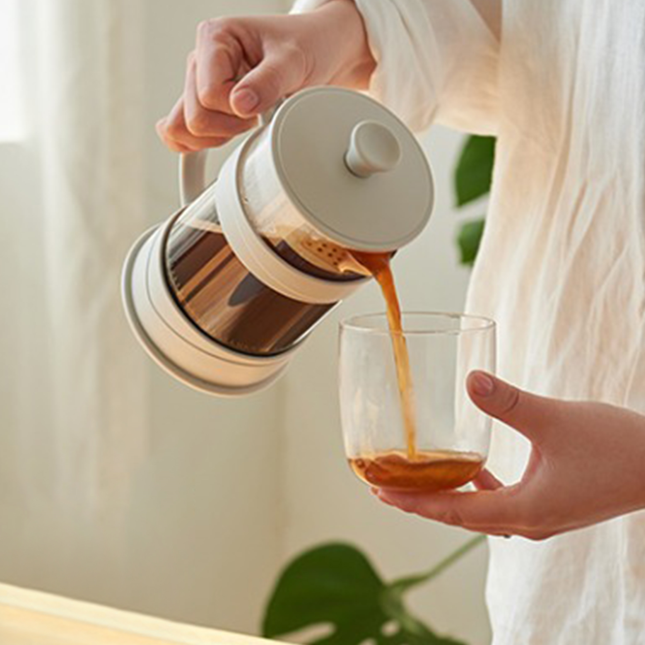 Person gießt Kaffee aus einer French Press in ein Glas. Der Kaffee ist dunkel.