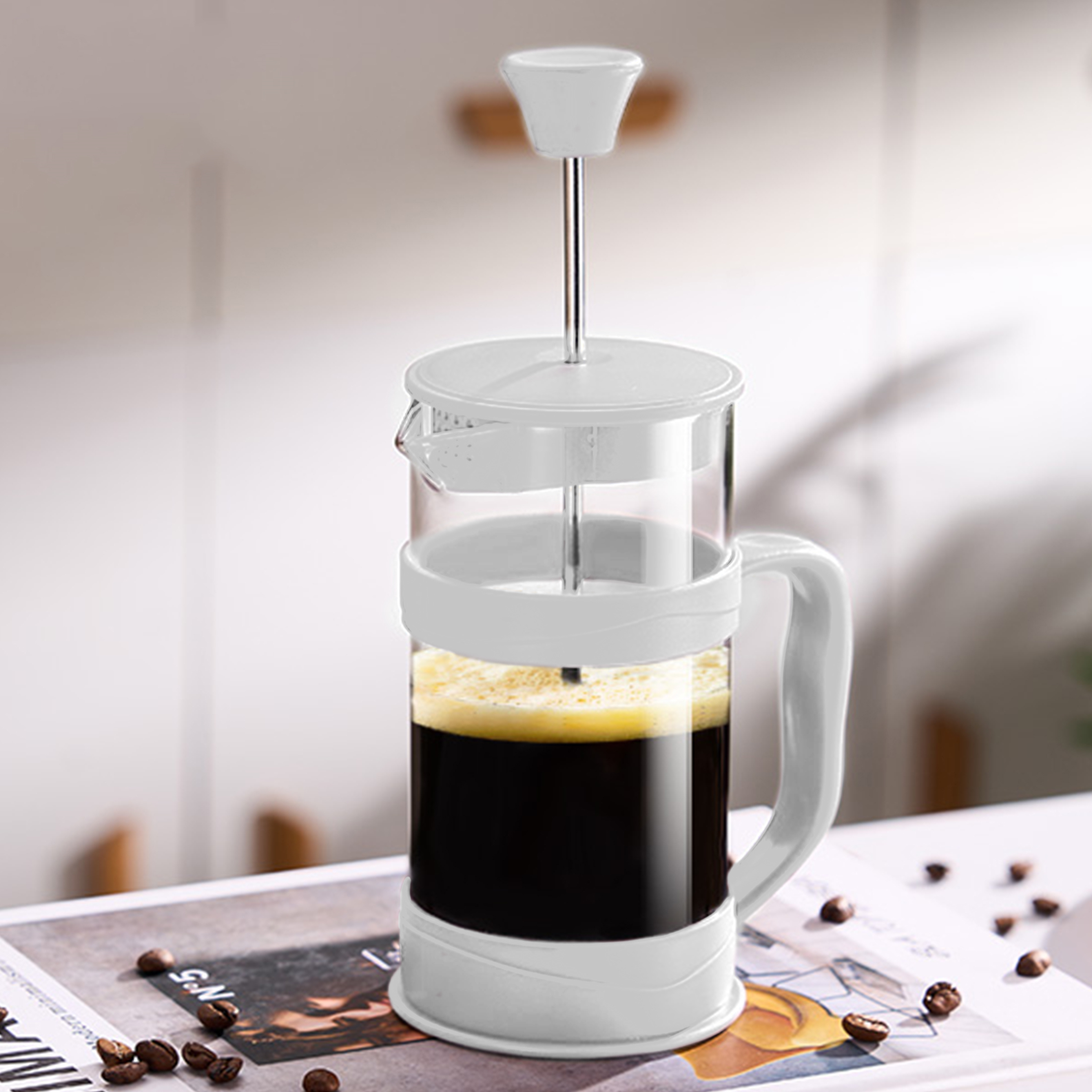 Eine French Press gefüllt mit Kaffee. Sie steht auf einer Oberfläche mit Kaffeebohnen und einer Zeitschrift.