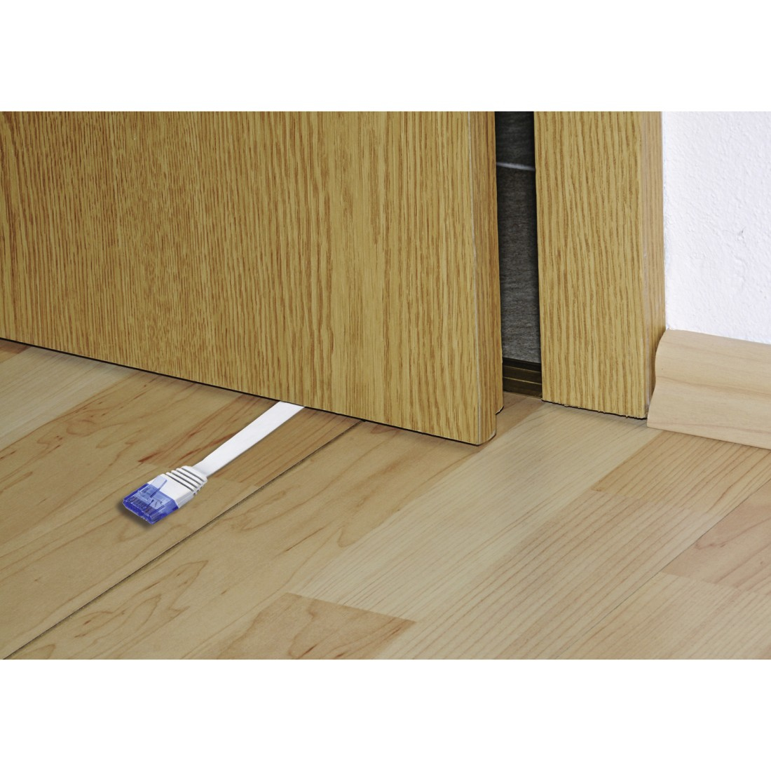 Cavo di rete bianco sotto una porta, con connettore blu a sinistra. Pavimento e porta in legno.