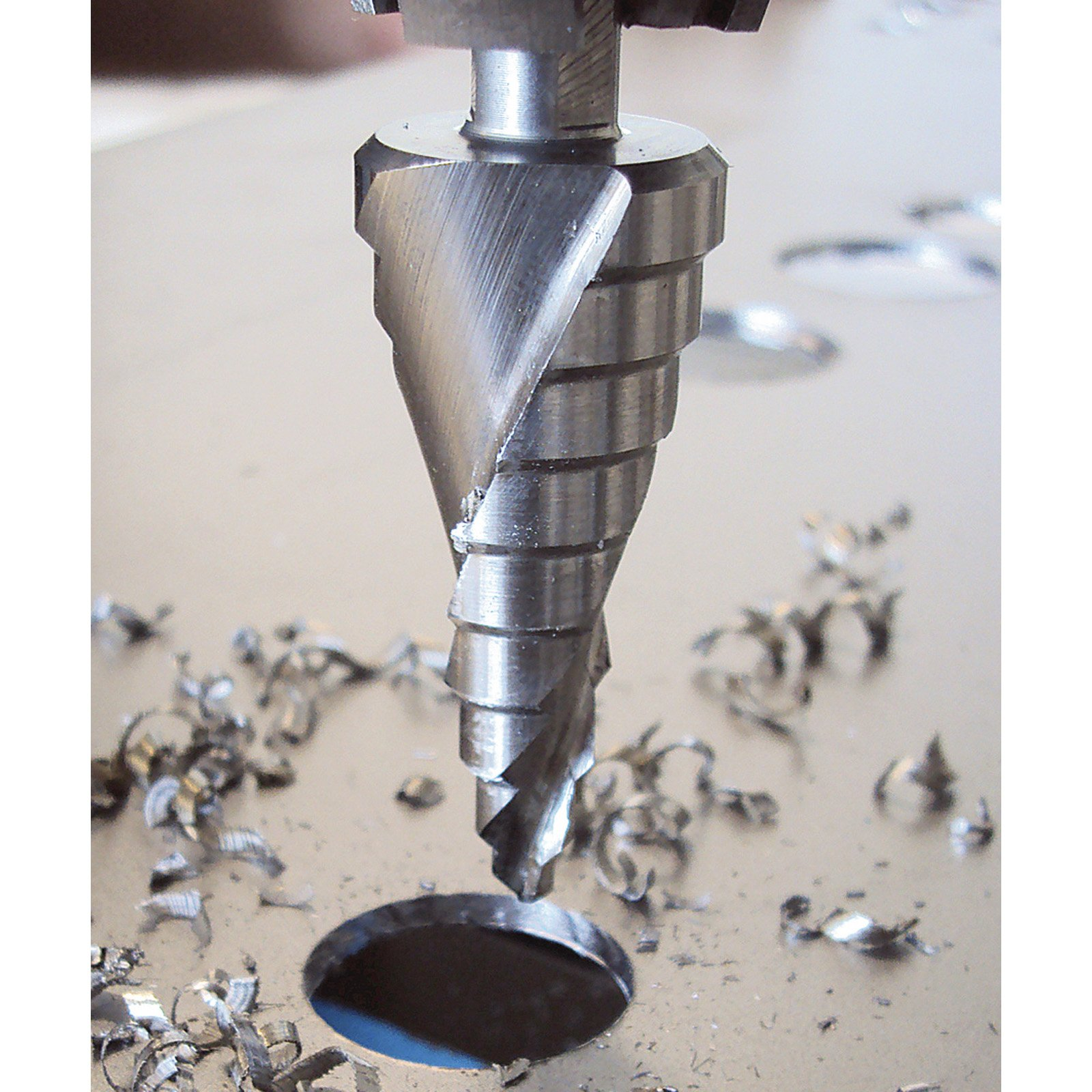 Ein Metall-Stufenbohrer, der ein Loch in ein Metallblech bohrt, mit Metallspänen drumherum.
