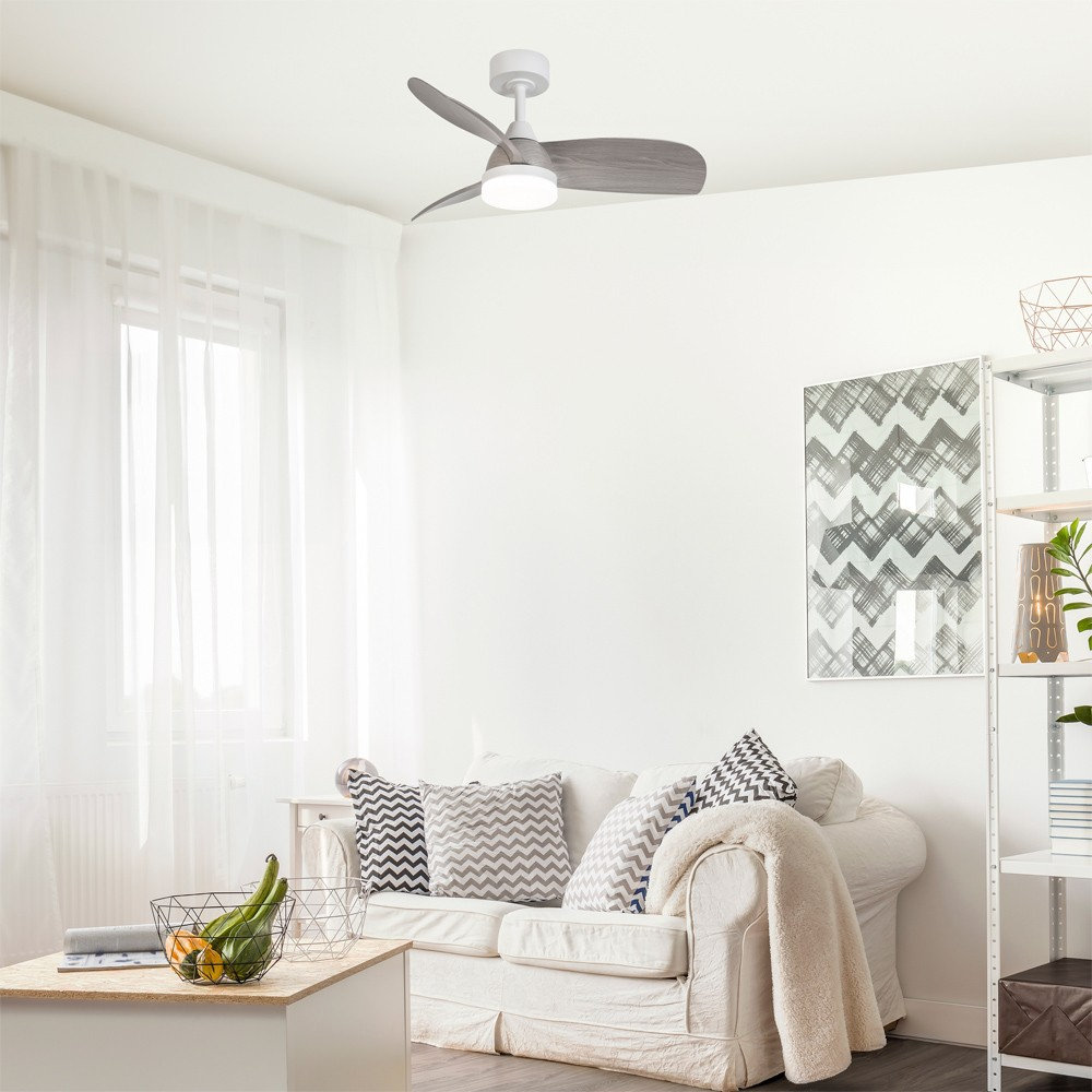 Un salón con ventilador de techo, paredes blancas, sofá y mesa con frutero.