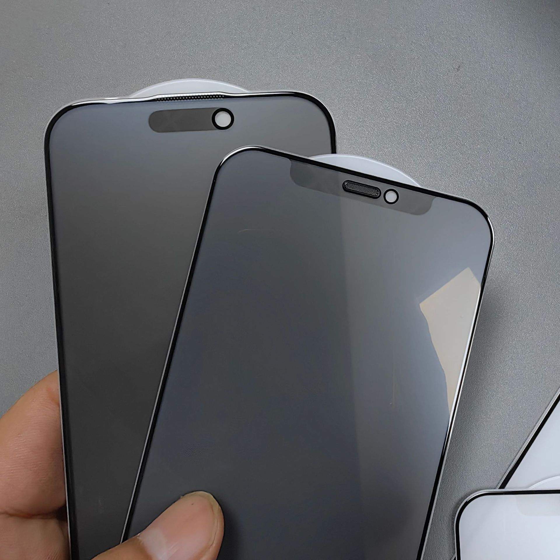 Dwie czarne osłony ekranu do telefonów na szarej powierzchni, trzymane przez dłoń.