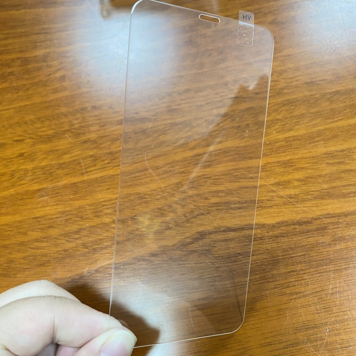Mano che tiene una protezione schermo trasparente per un telefono, su un tavolo di legno.