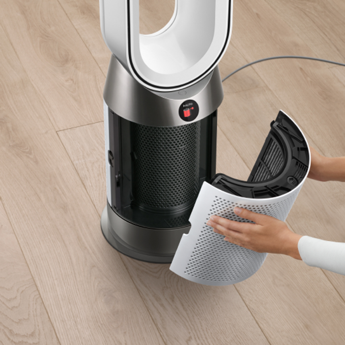 Persona quitando un filtro de un purificador de aire Dyson. El purificador es blanco y plateado.