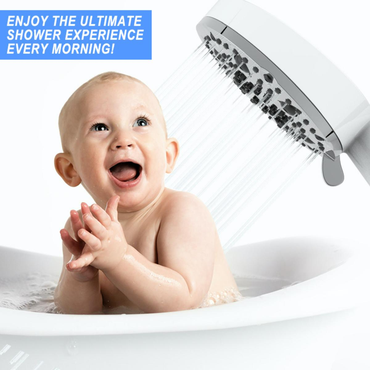 Ein Baby lächelt und blickt nach oben, wird mit Wasser aus einem Duschkopf in einer Badewanne besprüht.