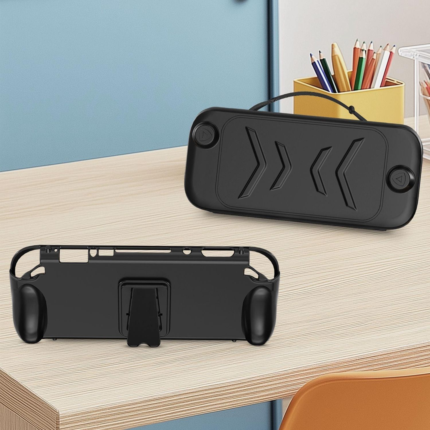 Eine schwarze Schutzhülle für ein Handheld-Spielgerät auf einem Schreibtisch, mit blauem Hintergrund und Stiften.