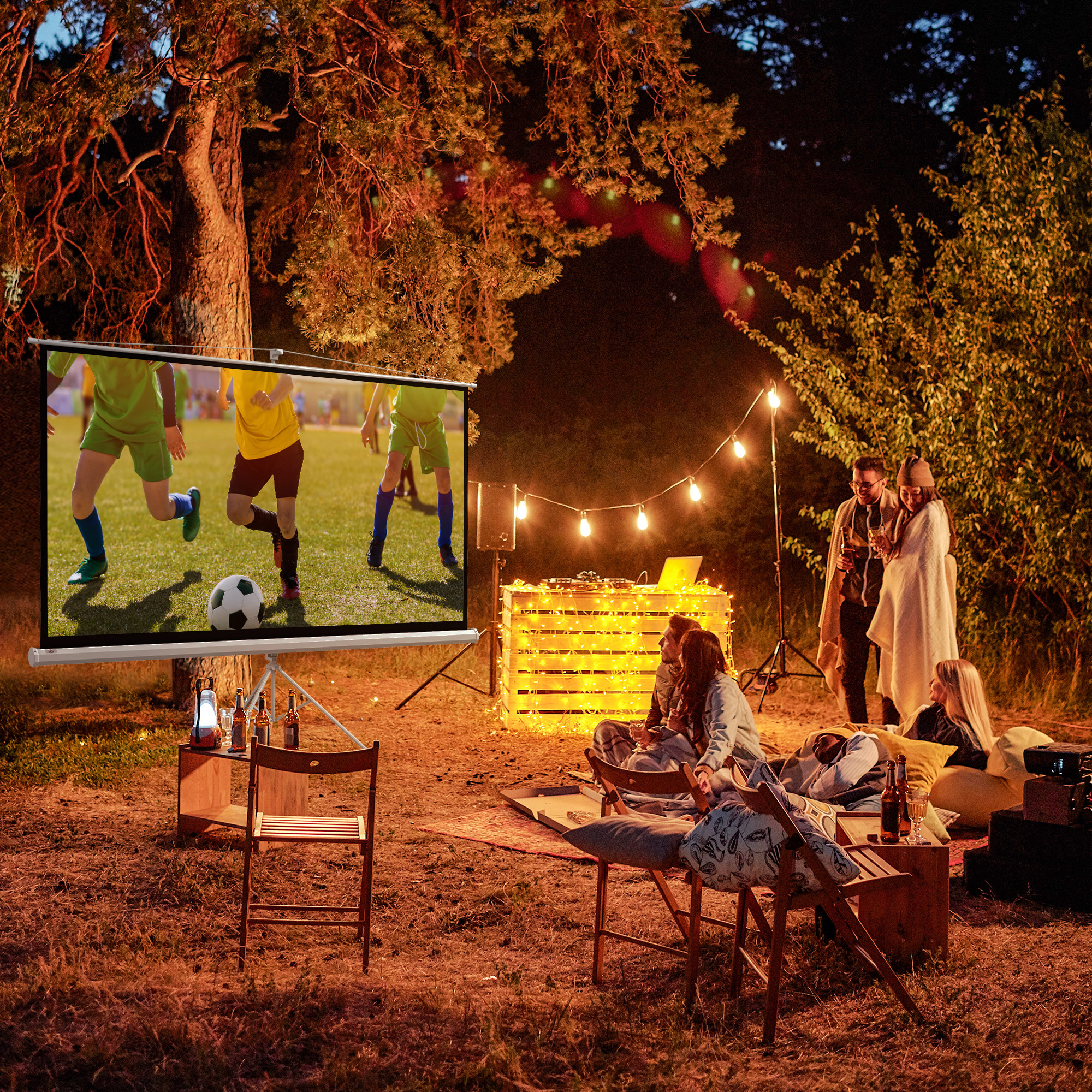 Persone che guardano una partita di calcio su uno schermo per proiettore in un parco, con luci e birre.