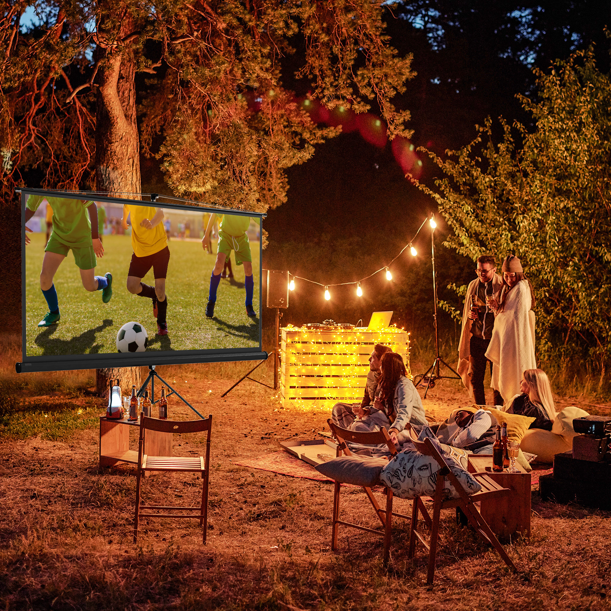 Persone che guardano una partita di calcio su uno schermo in un ambiente forestale notturno.
