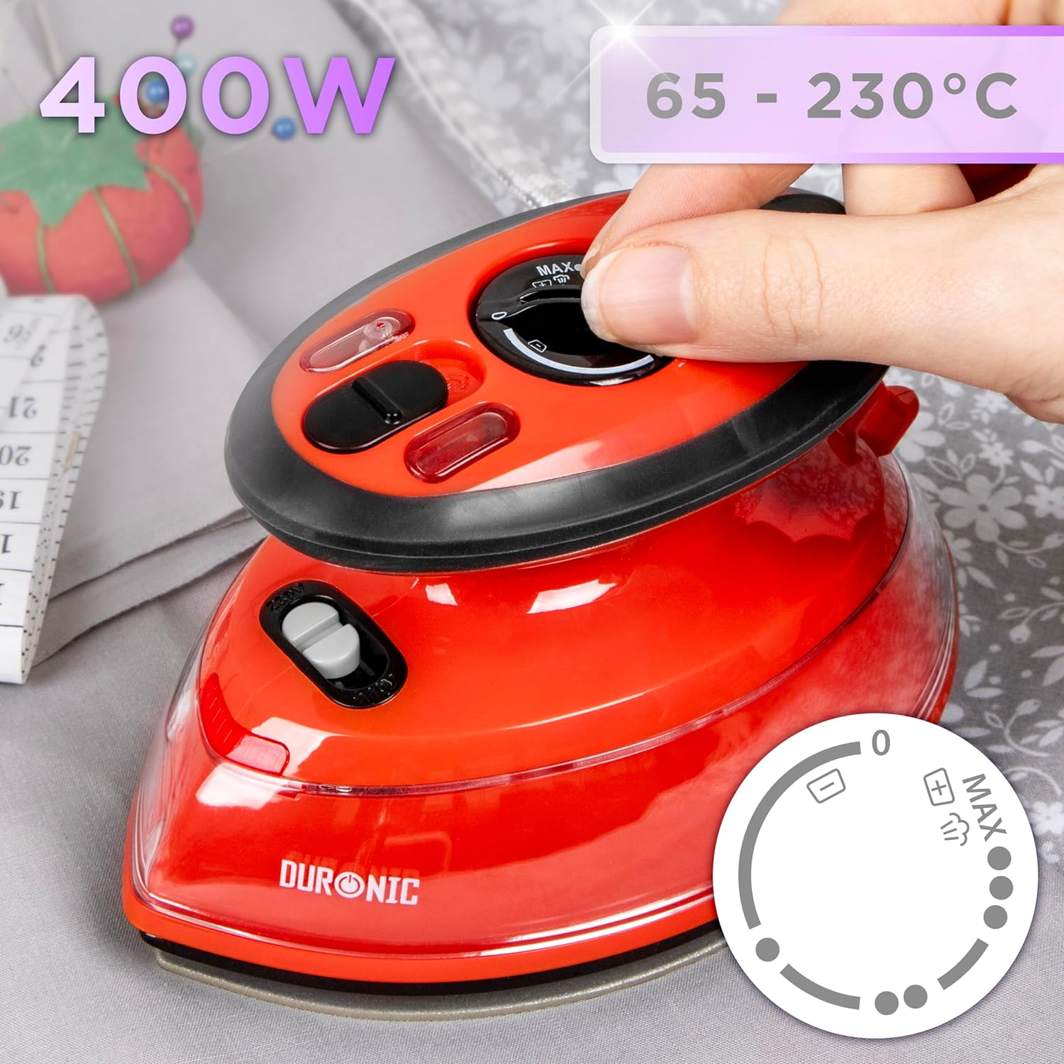 Rotes Bügeleisen mit einer Hand, die einen Drehregler einstellt. Stoffhintergrund mit Nähzubehör und Waage.