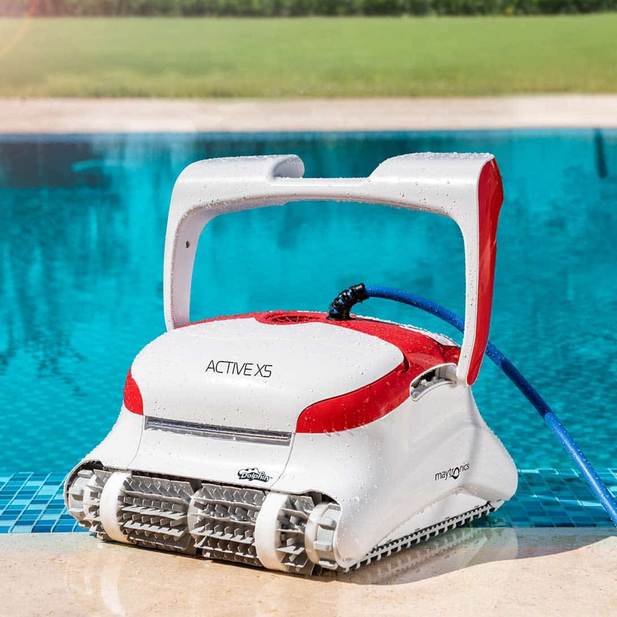 Robot limpiador de piscinas en el borde de una piscina. Blanco y rojo. La manguera está conectada. La piscina es azul.