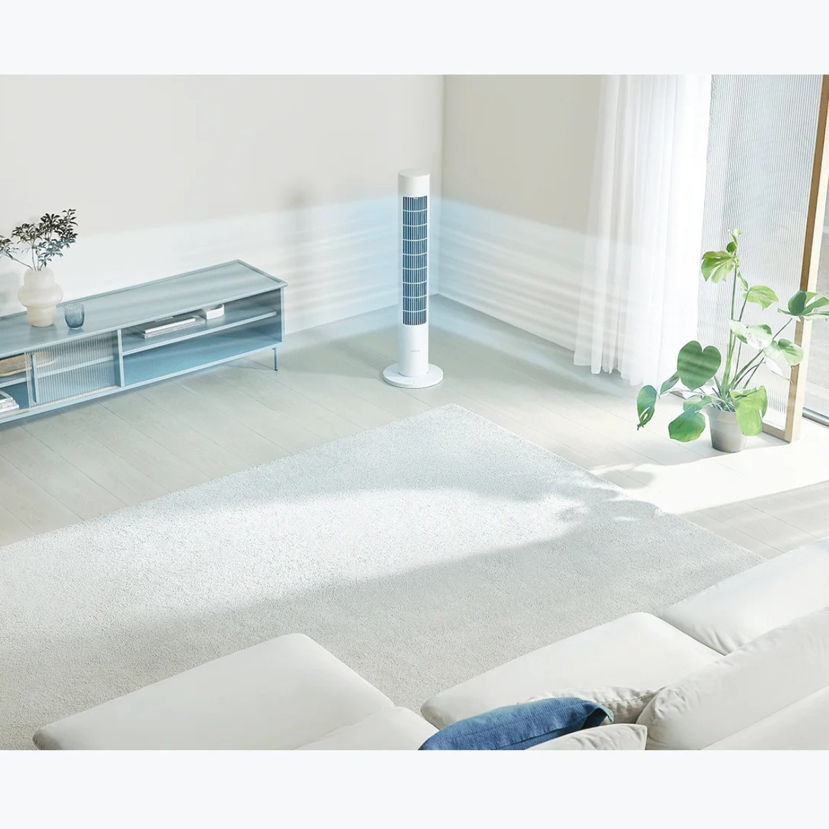 Biały wentylator wieżowy znajduje się w pokoju. Pokój ma białą sofę, dywan i roślinę.