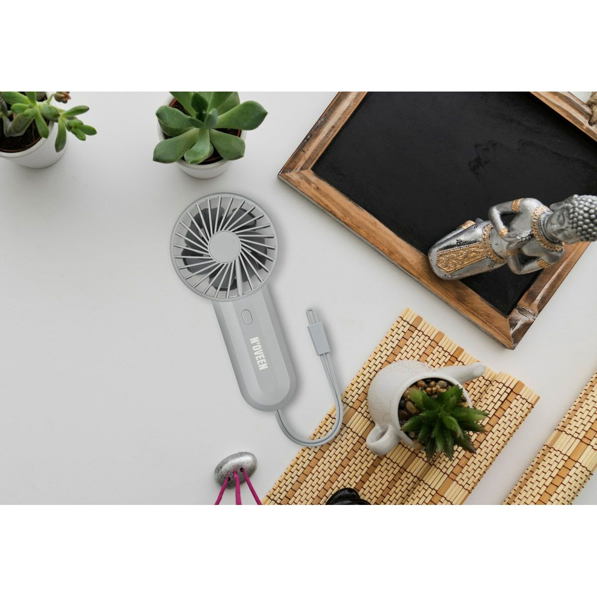 Szary mini wentylator, sukulenty, tablica, posąg Buddy i mata bambusowa na białej powierzchni.
