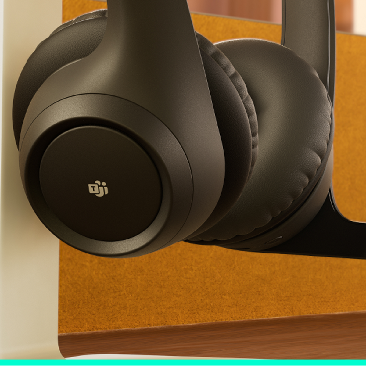 Zbliżenie ciemnych słuchawek wiszących na tle teksturowanego tła w kolorze opalenizny, ukazujące muszlę słuchawkową i pałąk.